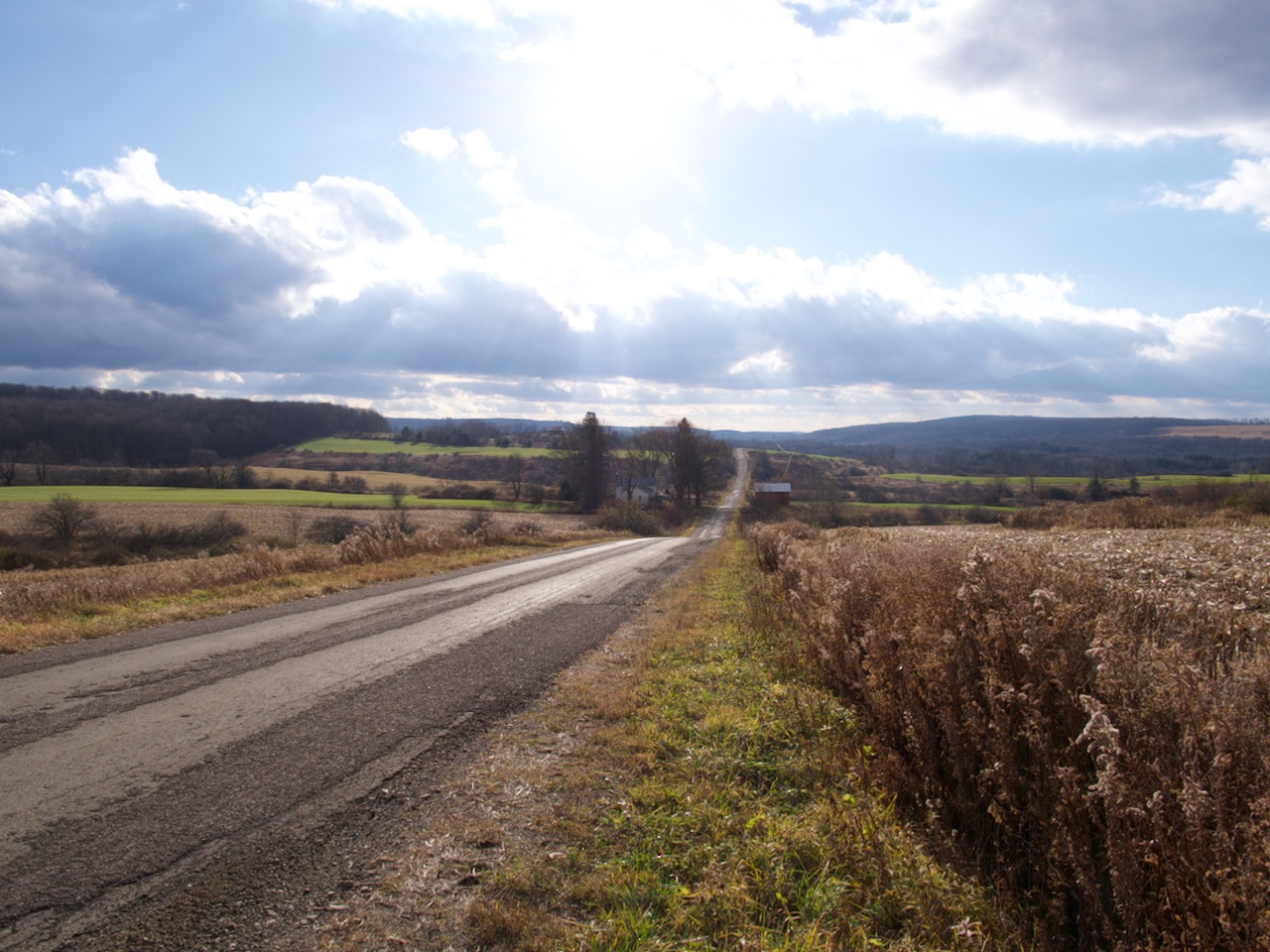 A country road in Cattaraugus County, NY, stretches to the horizon amid cornfields and a farmhouse in early winter (Nov. 2023)